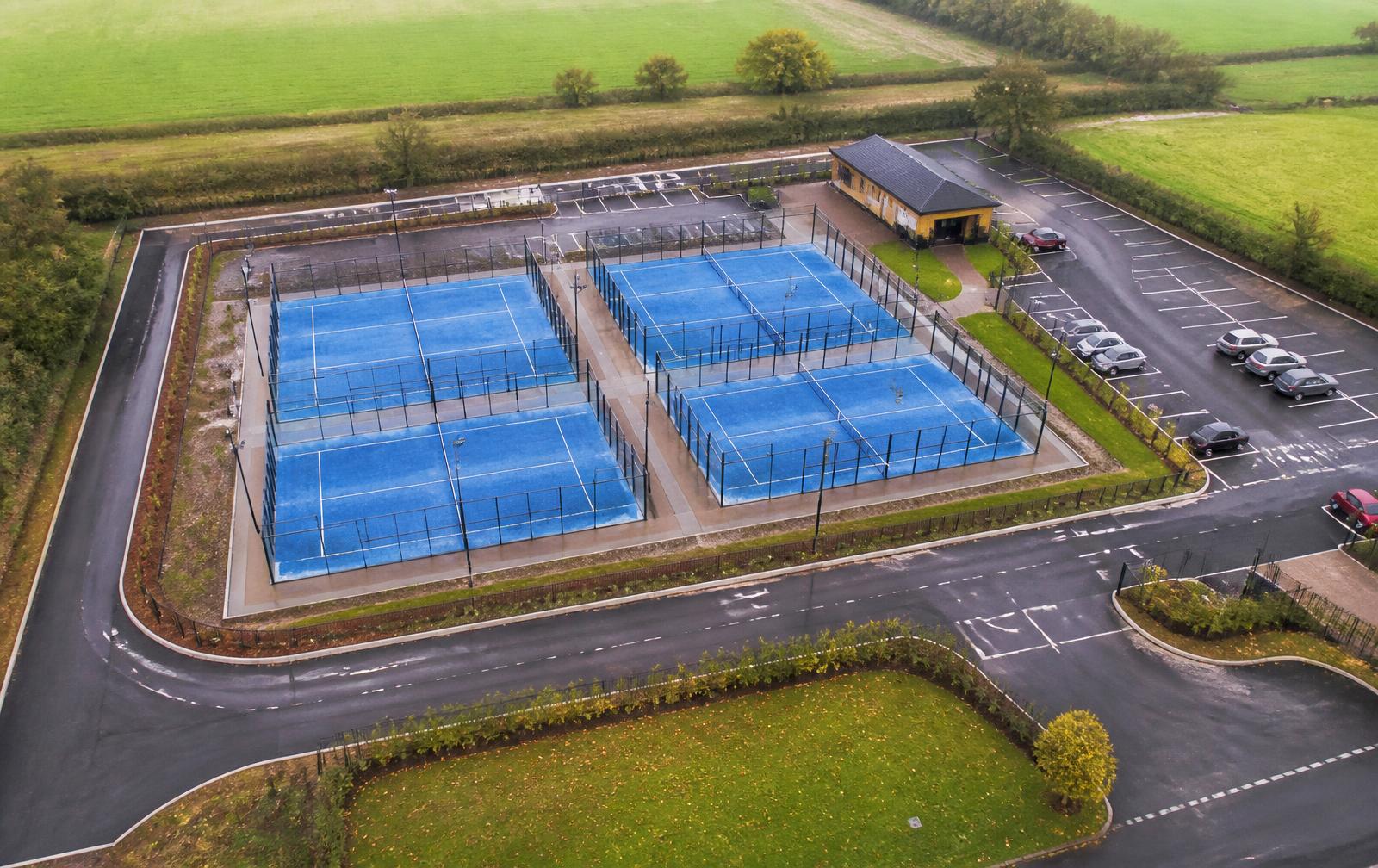 Aerial view of a multi-court padel development showing courts, access roads, parking, drainage and a clubhouse within a wider site